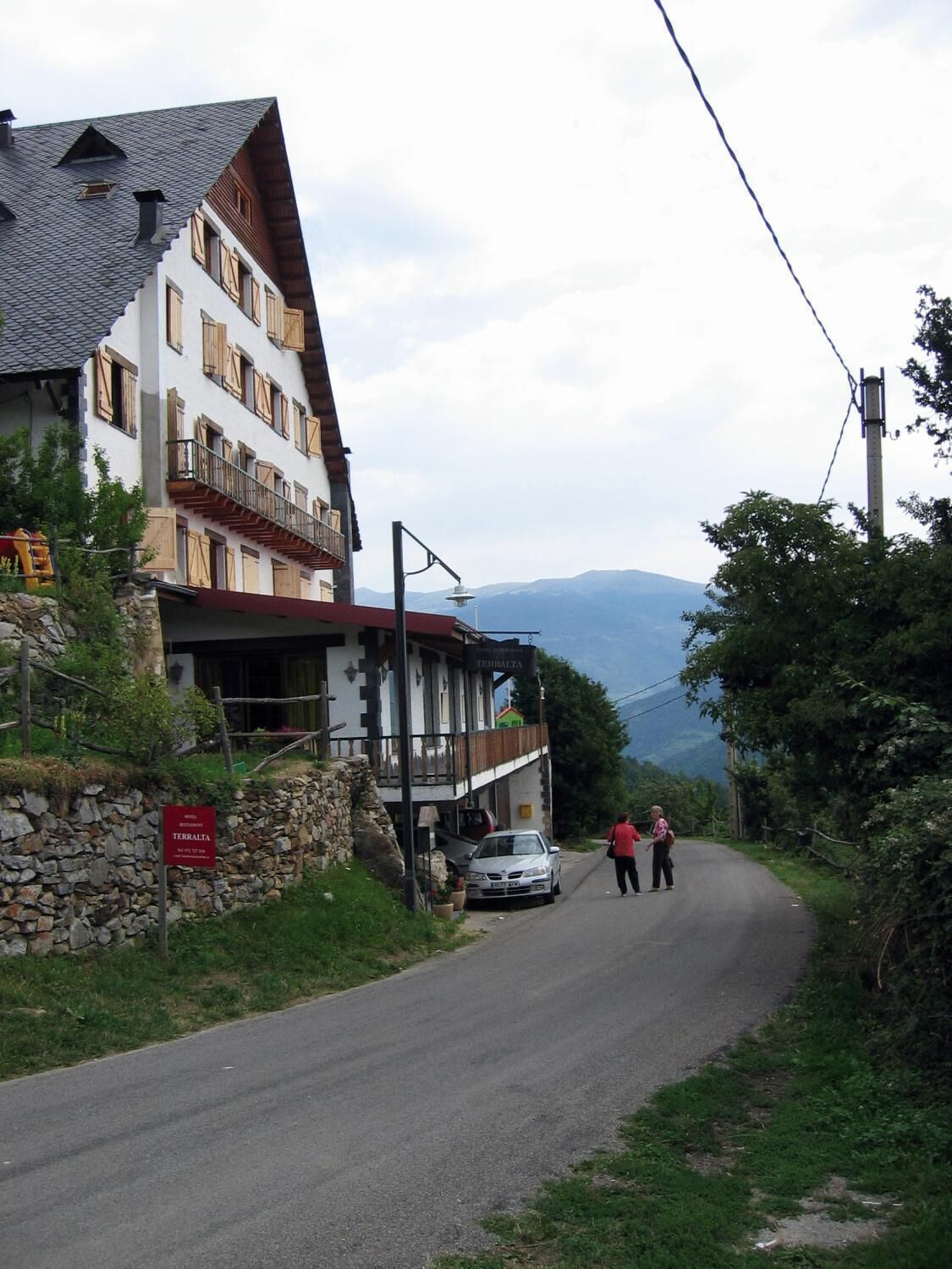 A traditional mountain hotel with a stone facade, wooden balconies, and a view of the mountains.