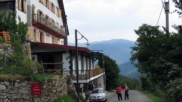 A traditional mountain hotel with a stone facade, wooden balconies, and a view of the mountains.