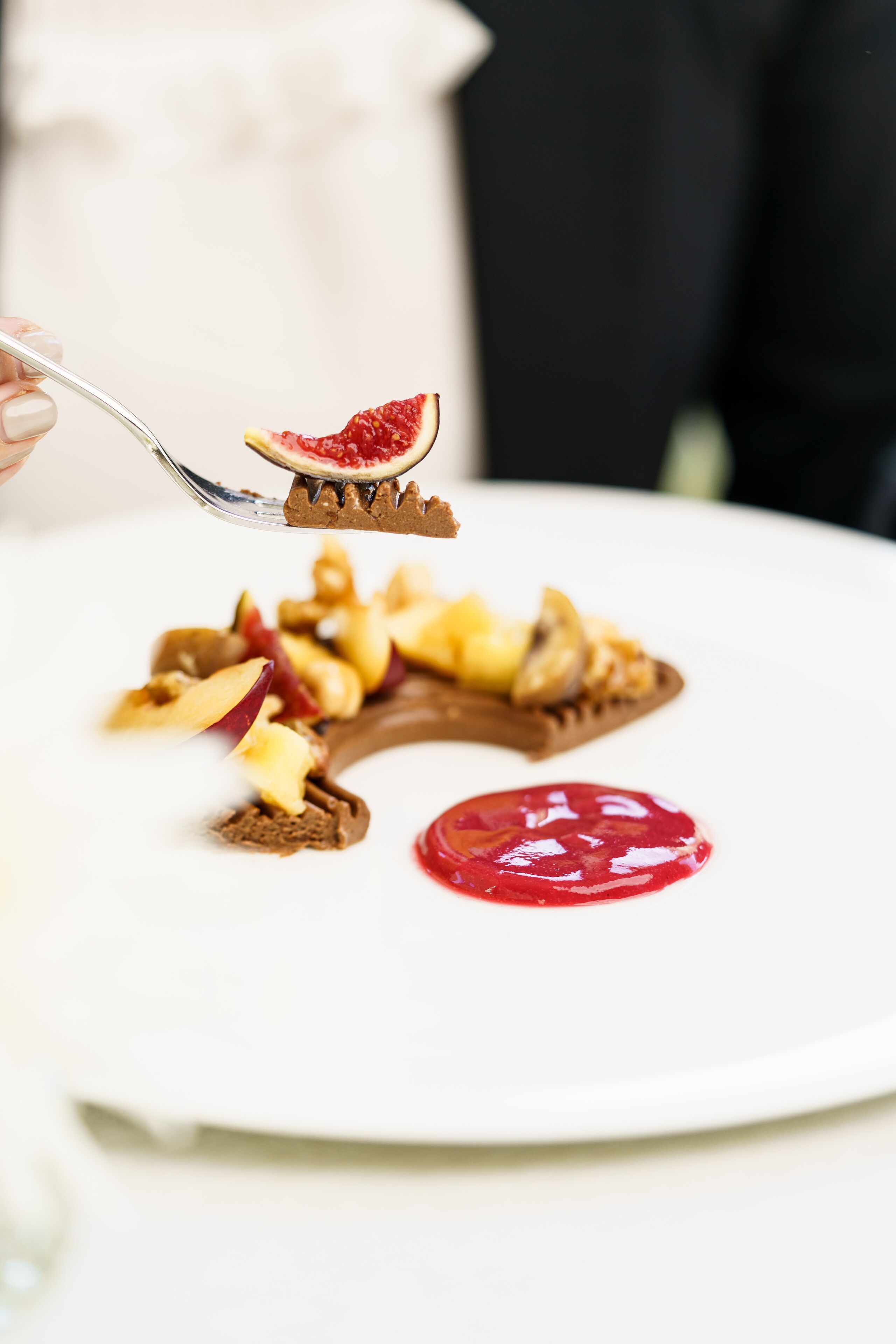 Une assiette blanche contenant un dessert au chocolat, des tranches de pomme et une sauce rouge.