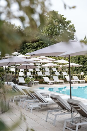 Un área junto a la piscina con sillones blancos y sombrillas.