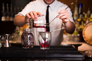 Un cantinero sirve una bebida en un vaso usando un colador.