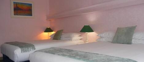 A hotel room with two beds, each with a pillow and a blanket. There are two bedside lamps.