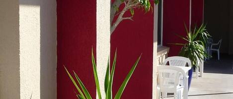 Un espacio al aire libre cubierto con paredes rojas, sillas blancas y plantas en macetas.