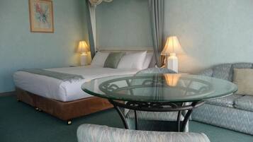 A hotel room with a bed, a glass table, a sofa, and two lamps.