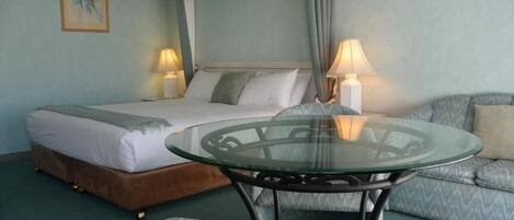 Una habitación de hotel con cama, una mesita de vidrio, un sofá y dos lámparas.