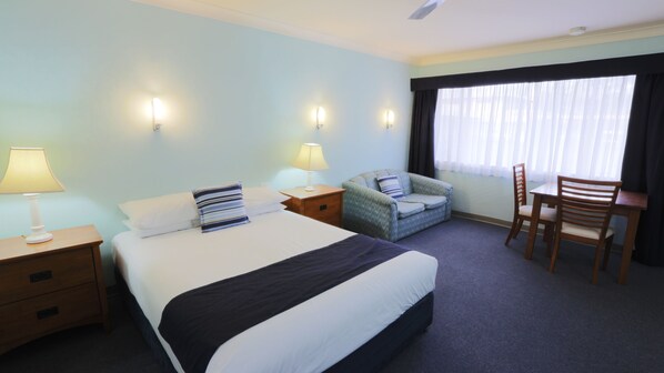 A hotel room with a large bed, two bedside tables with lamps, a chair, a small table, and a window with curtains. - Tweed Heads Vegas Motel (Tweed Heads)