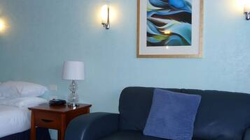 A room with a bed, a small table with a lamp, a couch, and a painting on the wall.