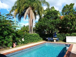 A rectangular swimming pool with a tiled edge, surrounded by lush greenery and trees. - Tweed Heads Vegas Motel (Tweed Heads)