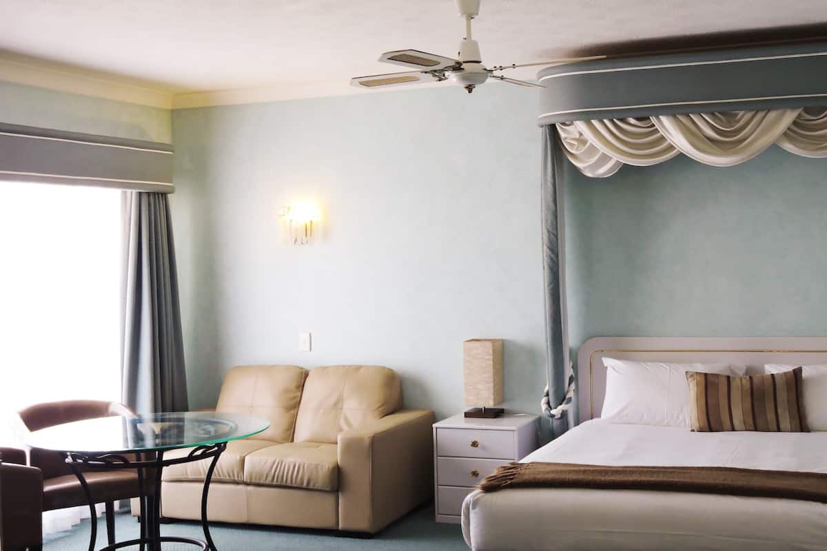 A hotel room with a bed, a glass table, a sofa, a nightstand, and a ceiling fan.
