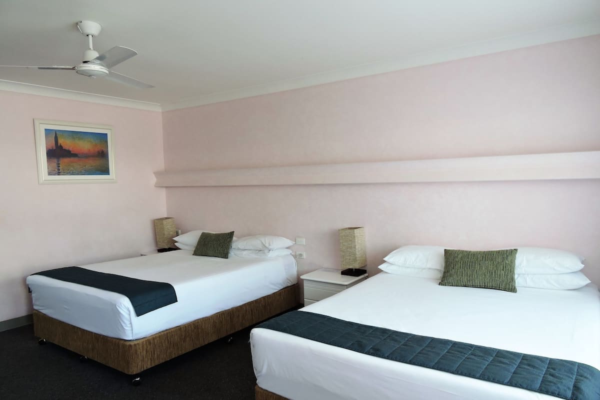 A hotel room with two beds, a ceiling fan, a painting on the wall, and a nightstand with a lamp.