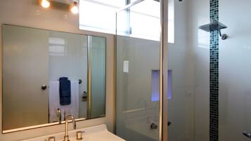 A modern bathroom with a glass-enclosed shower, a large mirror, and a white sink.