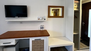 A modern hotel room with a wooden desk, a flat-screen TV, a small shelf with toiletries, a woven basket, and a wardrobe with a mirror. - Hotel Gumusluk (Bodrum)