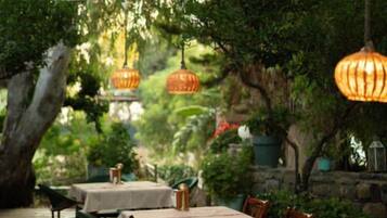 Un área de comedor al aire libre con mesas y sillas, cubierta por un toldo y faroles colgantes.
