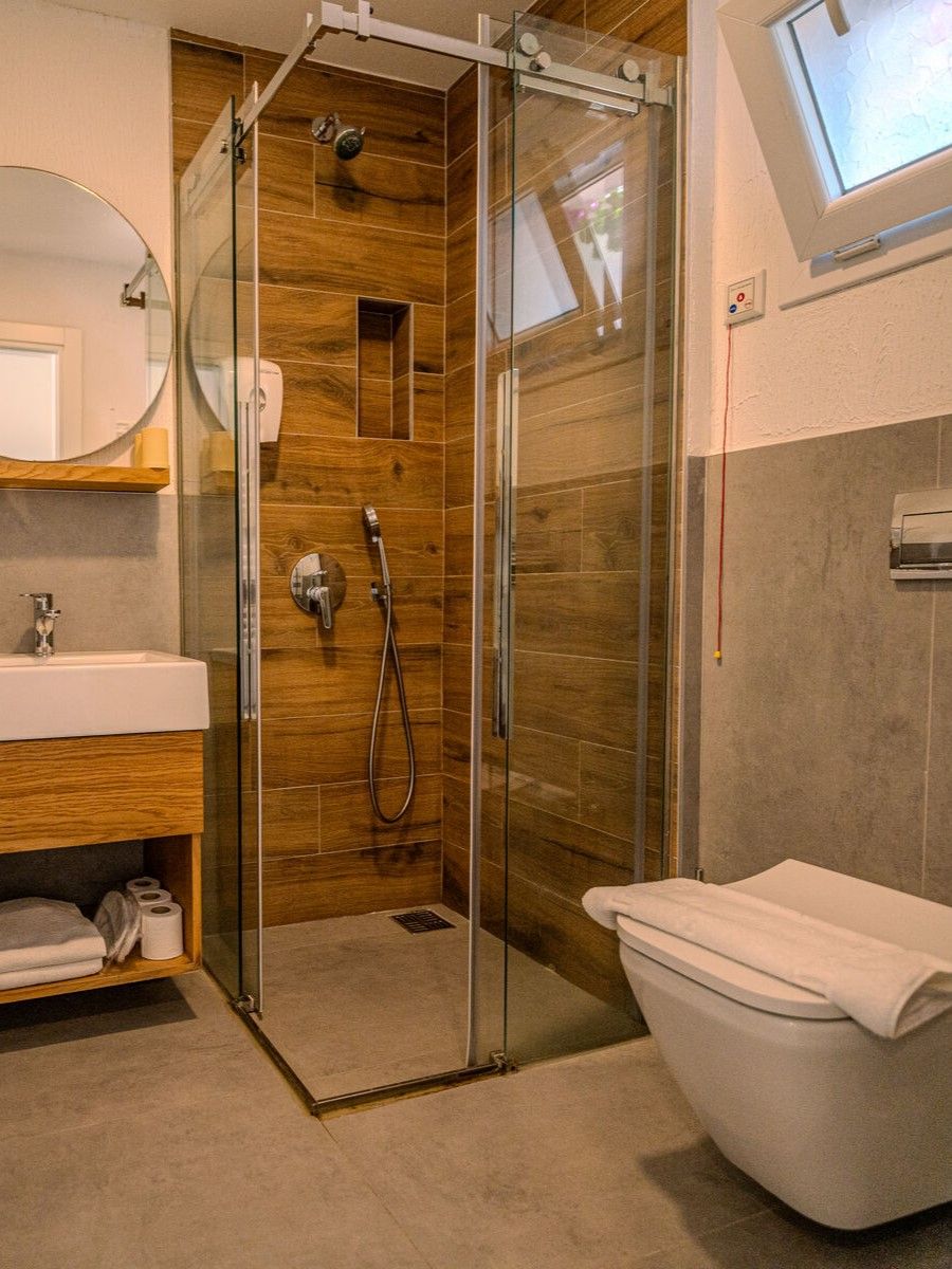 A modern bathroom with a glass-enclosed shower, a white toilet, and a wooden vanity with a mirror.