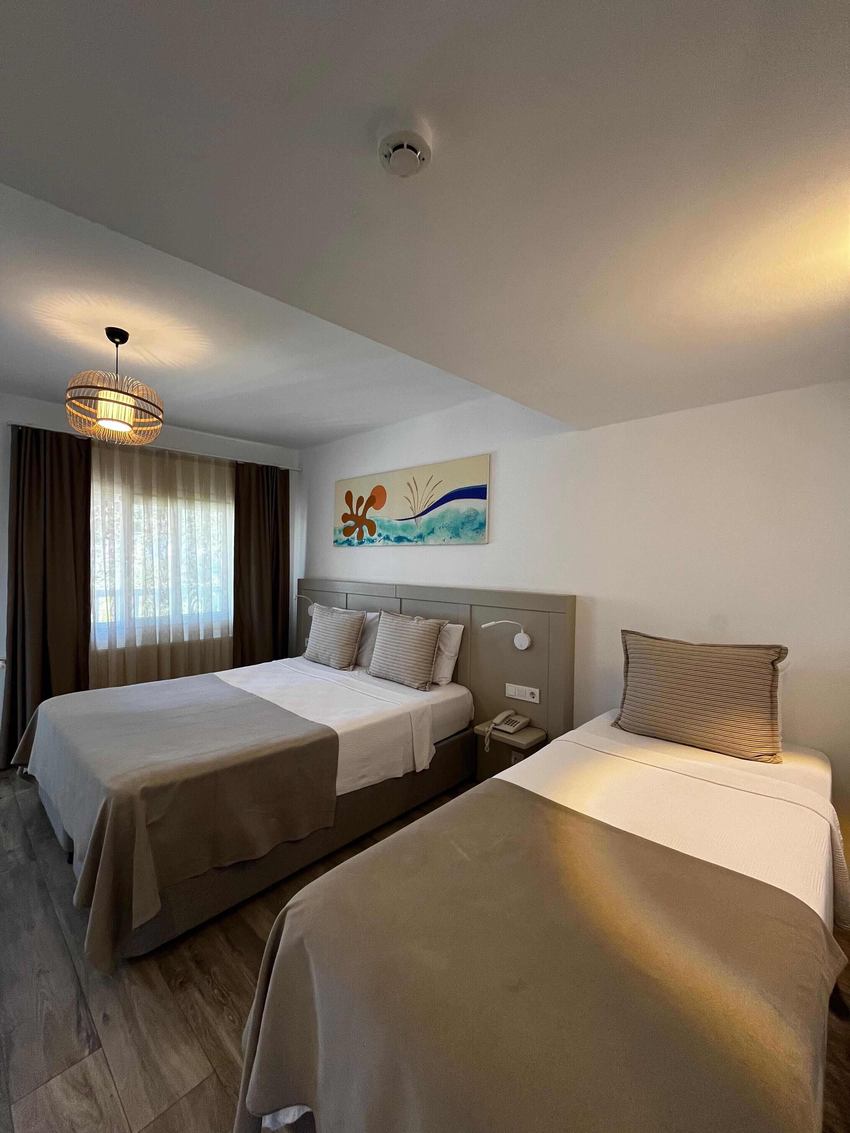 A hotel room with two beds, a painting, a phone on the nightstand, and a ceiling light.
