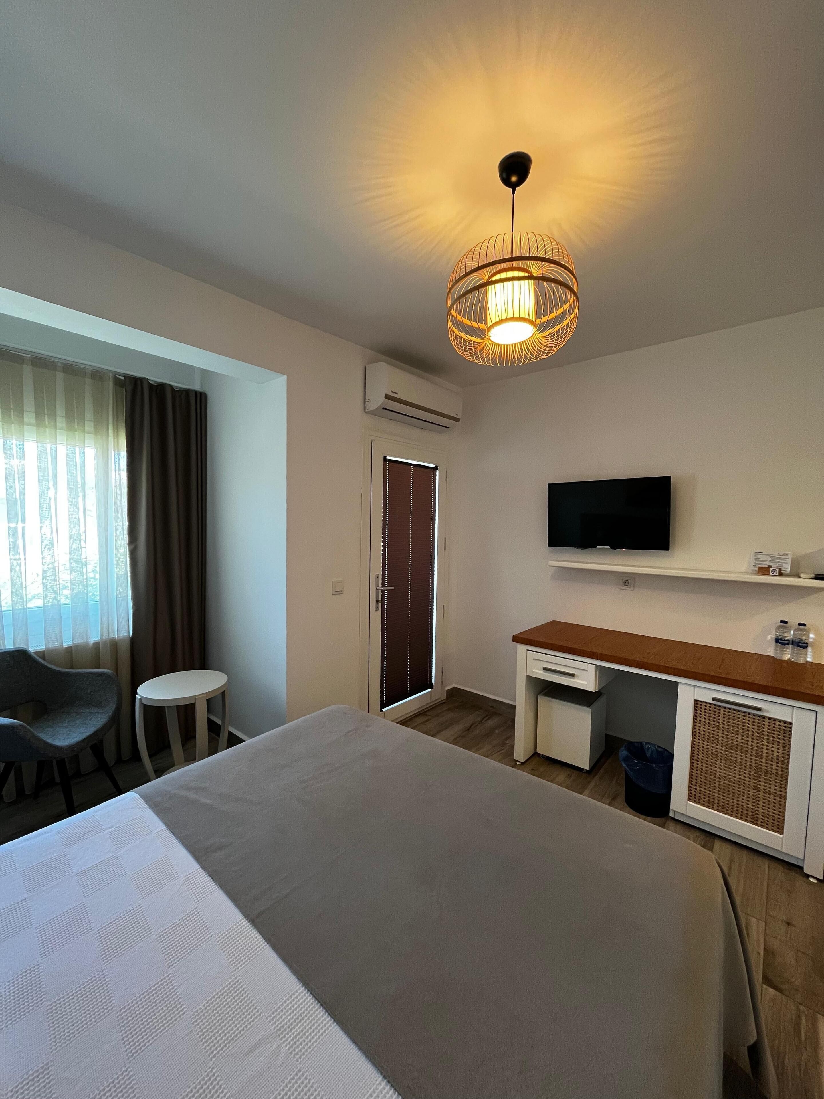 Habitación de hotel con cama, escritorio, silla, televisor y aire acondicionado.
