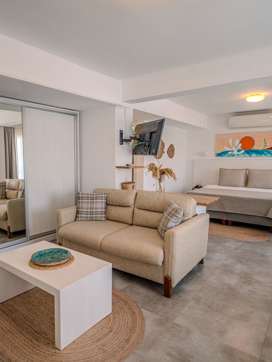Een moderne woonkamer met een beige bank, een witte salontafel en een aan de muur bevestigde televisie.