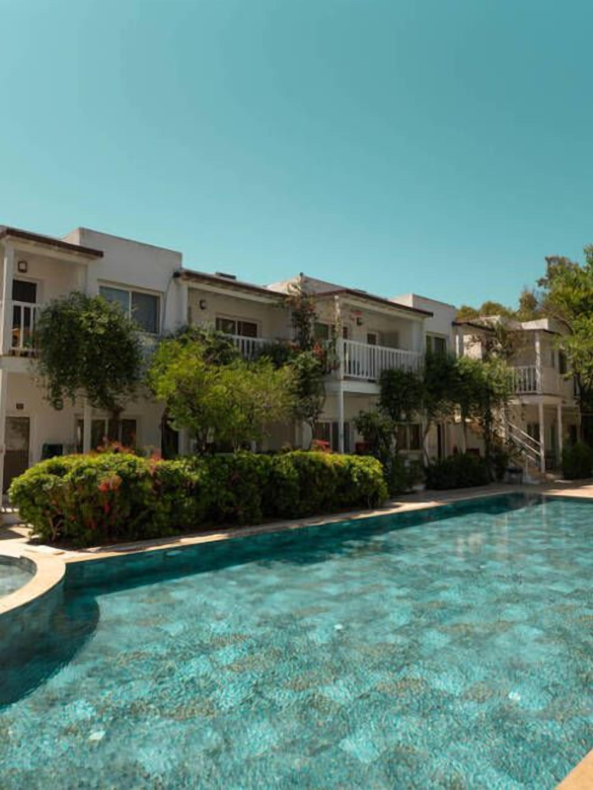 Une piscine entourée d’un bâtiment doté de balcons et de verdure.