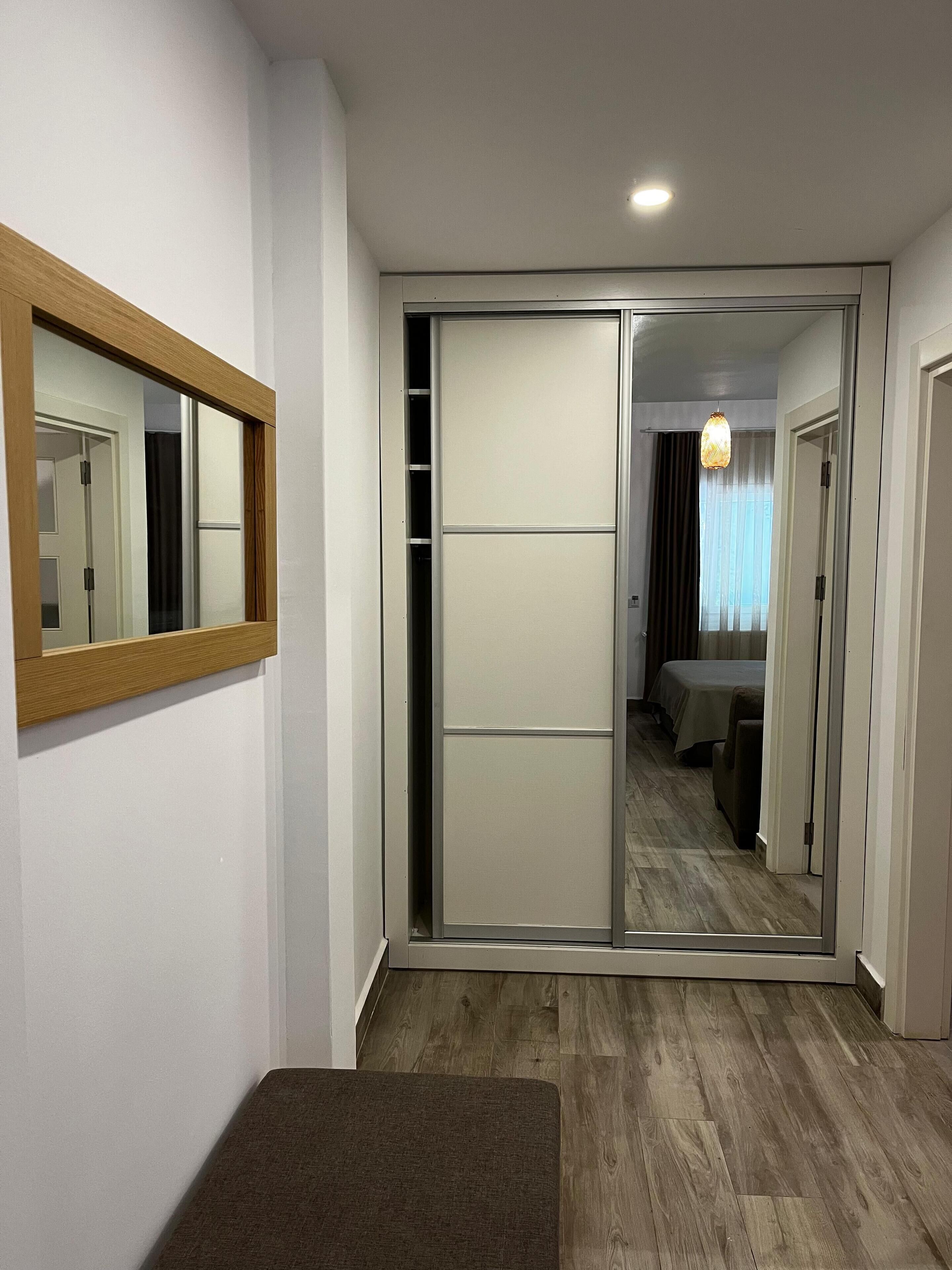 A hotel room with a sliding door leading to a bedroom, a bedside table, and a mirror on the wall.