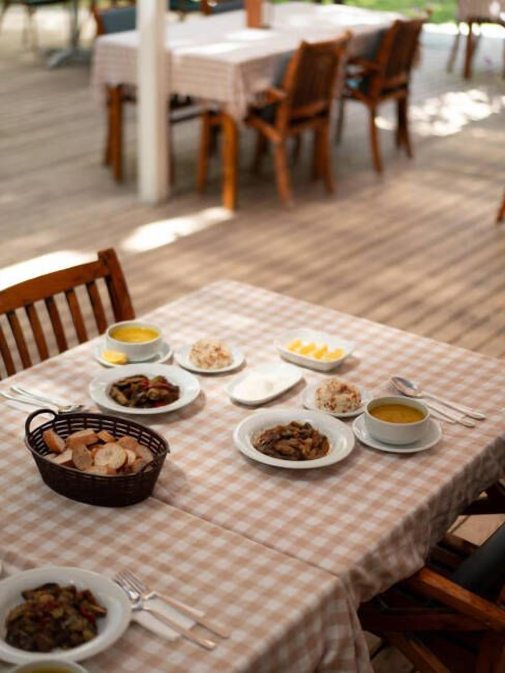 An outdoor dining area with a checkered tablecloth, various dishes, and wooden chairs.