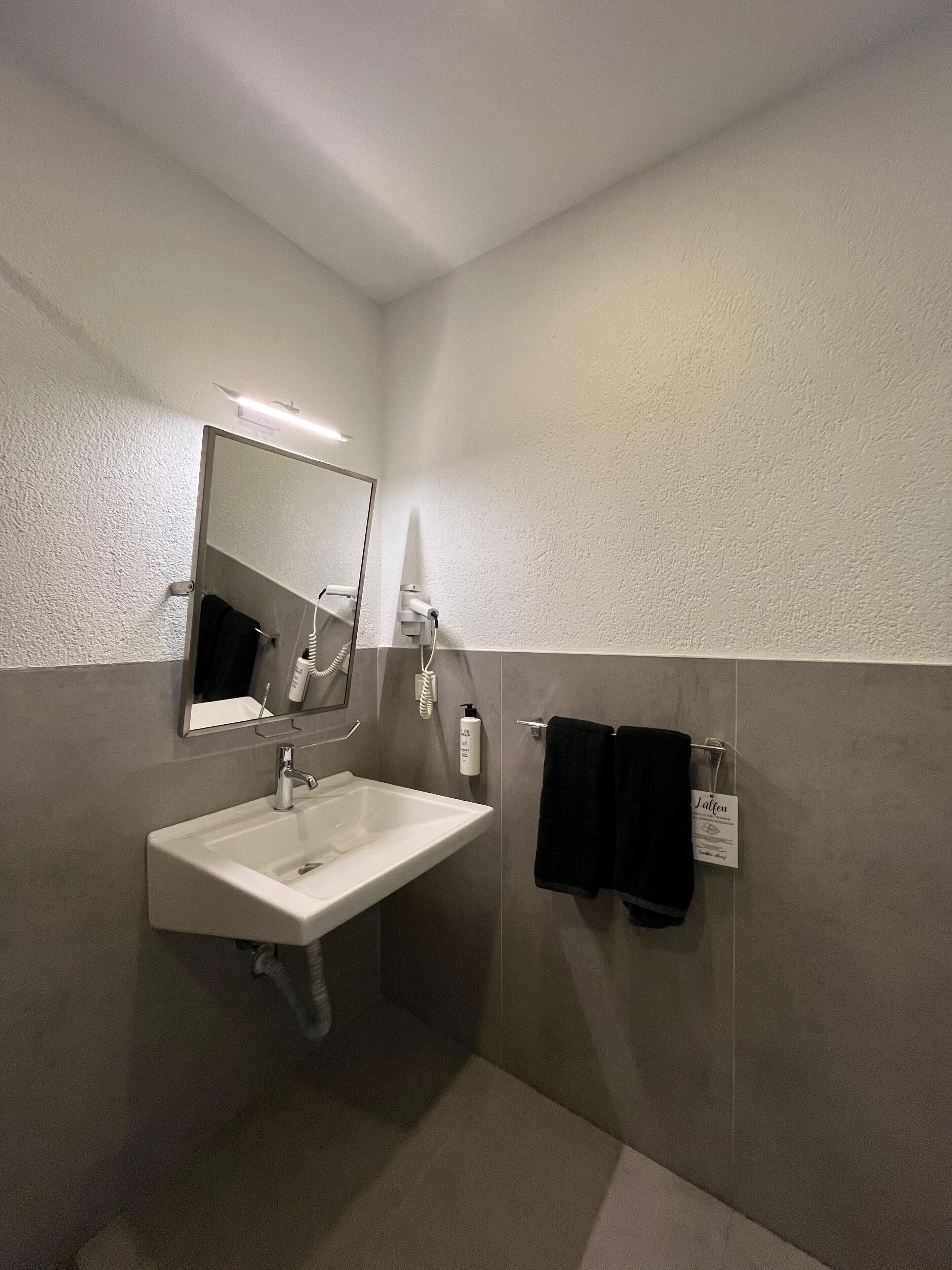 A modern bathroom with a white sink, a mirror, and a towel rack.