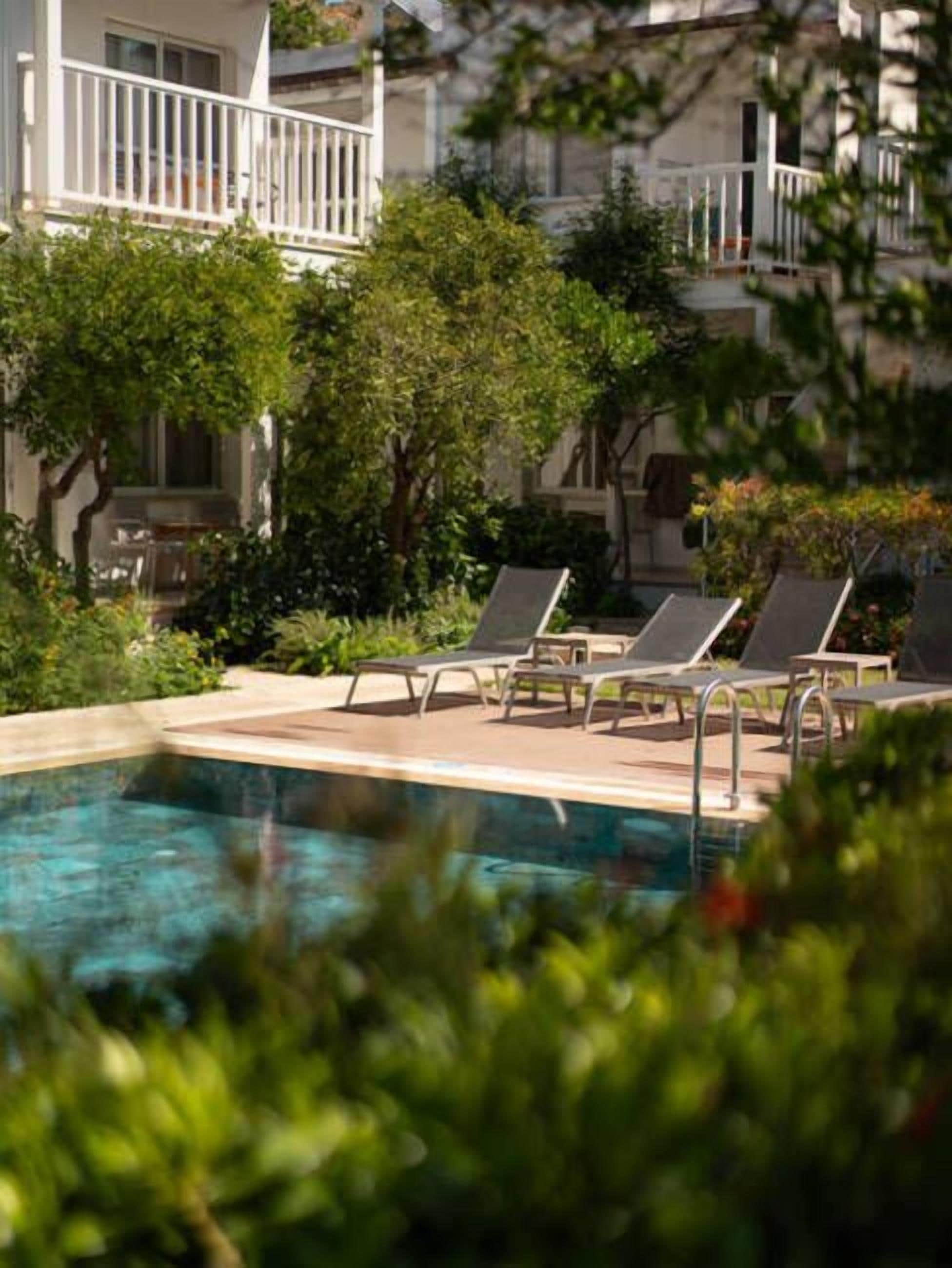 A swimming pool with lounge chairs, surrounded by greenery and a building with balconies.