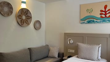 A modern hotel room with a sofa, two single beds, a wall-mounted lamp, and a painting.