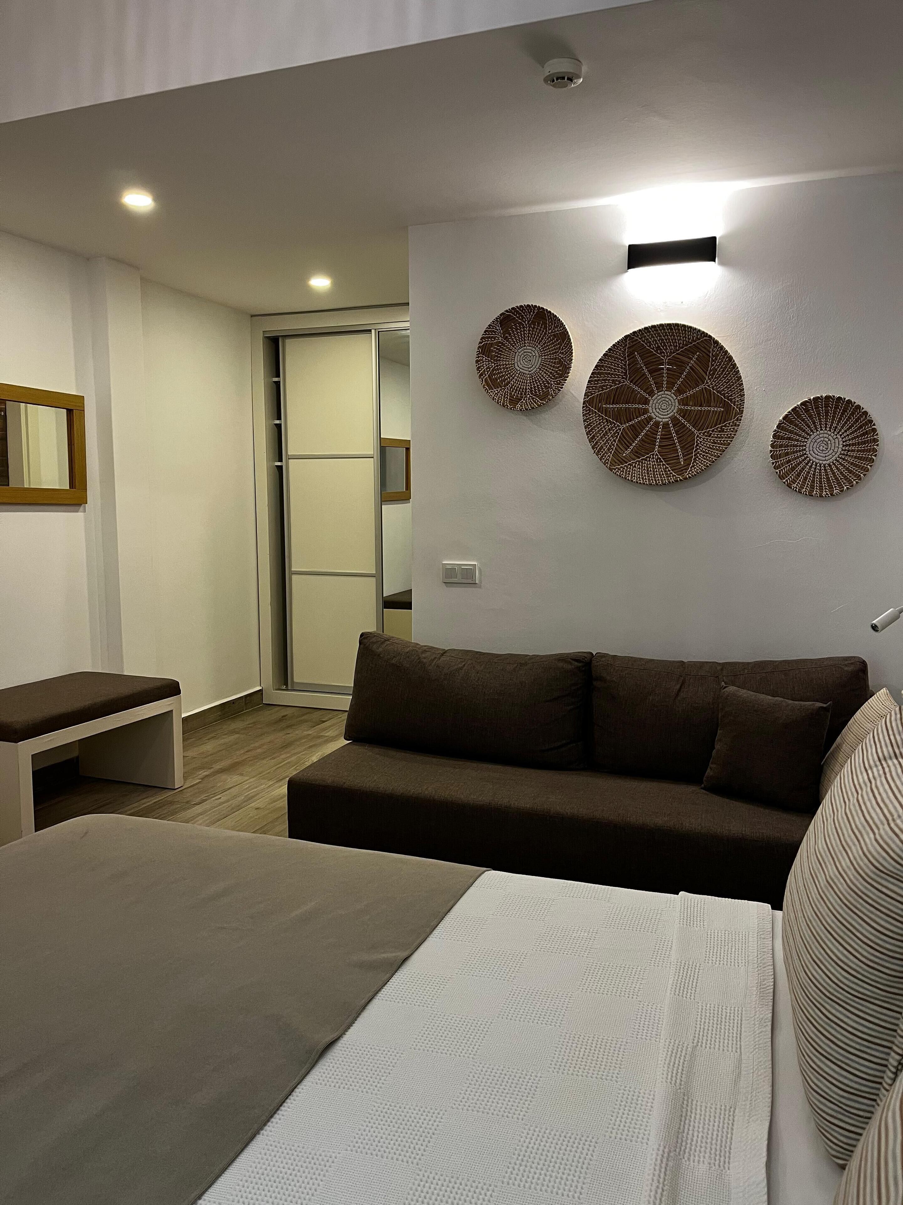 A modern hotel room with a bed, a sofa, a bench, and decorative wall art.