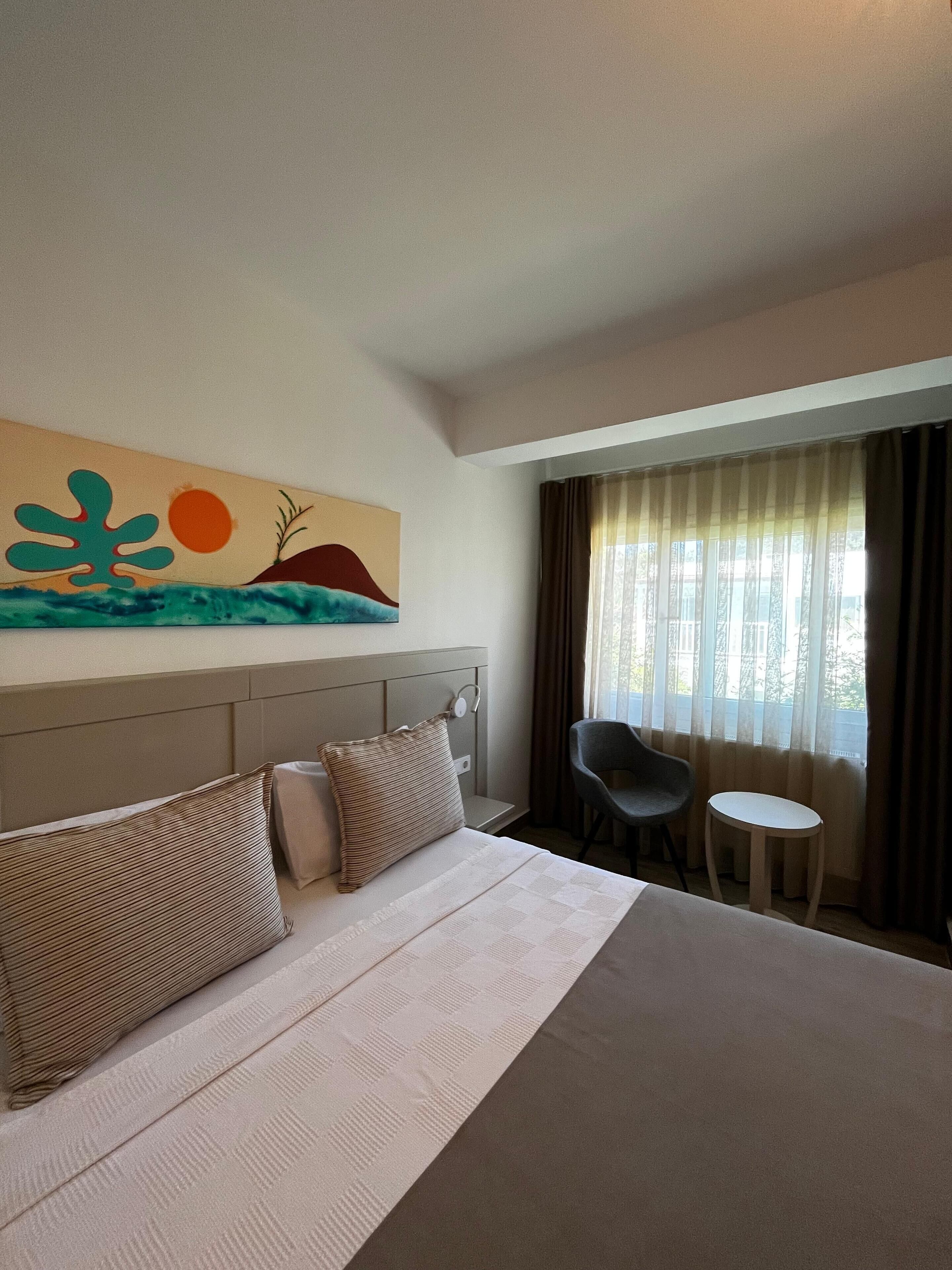 Een hotelkamer met een groot bed, een bureau, een stoel en een schilderij aan de muur.