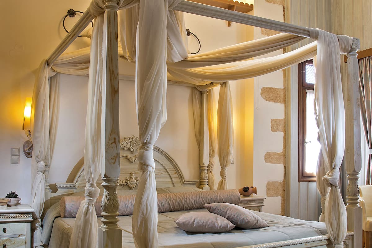 A four-poster canopy bed with a wooden headboard, a bedside table with a lamp, and a nightstand.