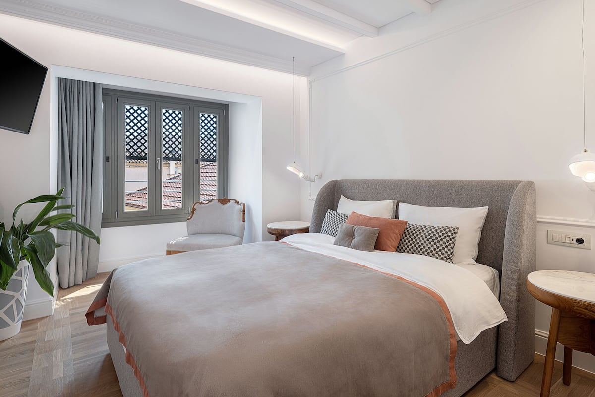 A hotel room with a large bed, a chair, a bedside table, a lamp, and a potted plant.