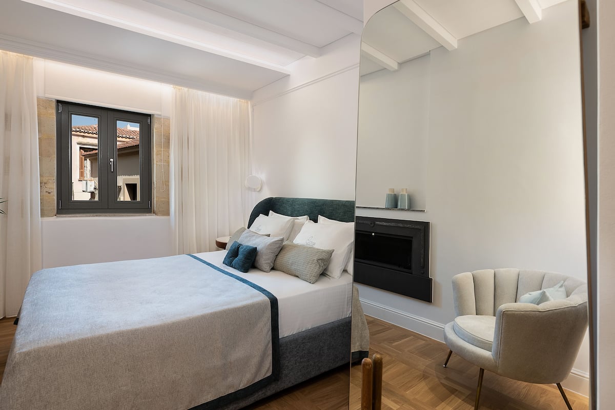 A bedroom with a bed, a chair, a mirror, and a window.