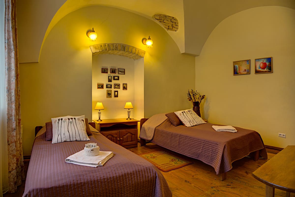 A hotel room with two beds, a wooden desk, two lamps, and a wall with framed pictures.