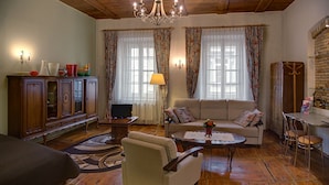 A cozy living room with a sofa, armchair, wooden cabinet, and a dining area with a table and chairs. - Bernardinu B&B House (Vilnius)