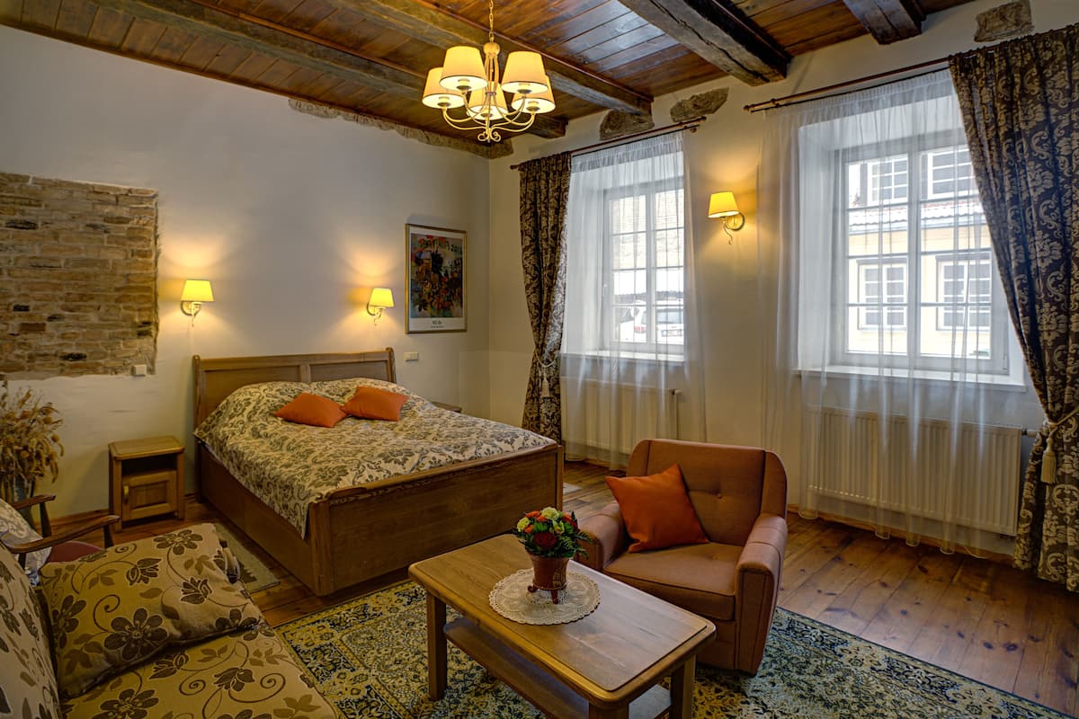 A cozy bedroom with a wooden bed, a small table, a chair, and a window with curtains.