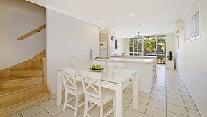 A modern kitchen with a glass dining table, white cabinetry, and a wooden staircase. - Portside Noosa Waters (Noosaville)