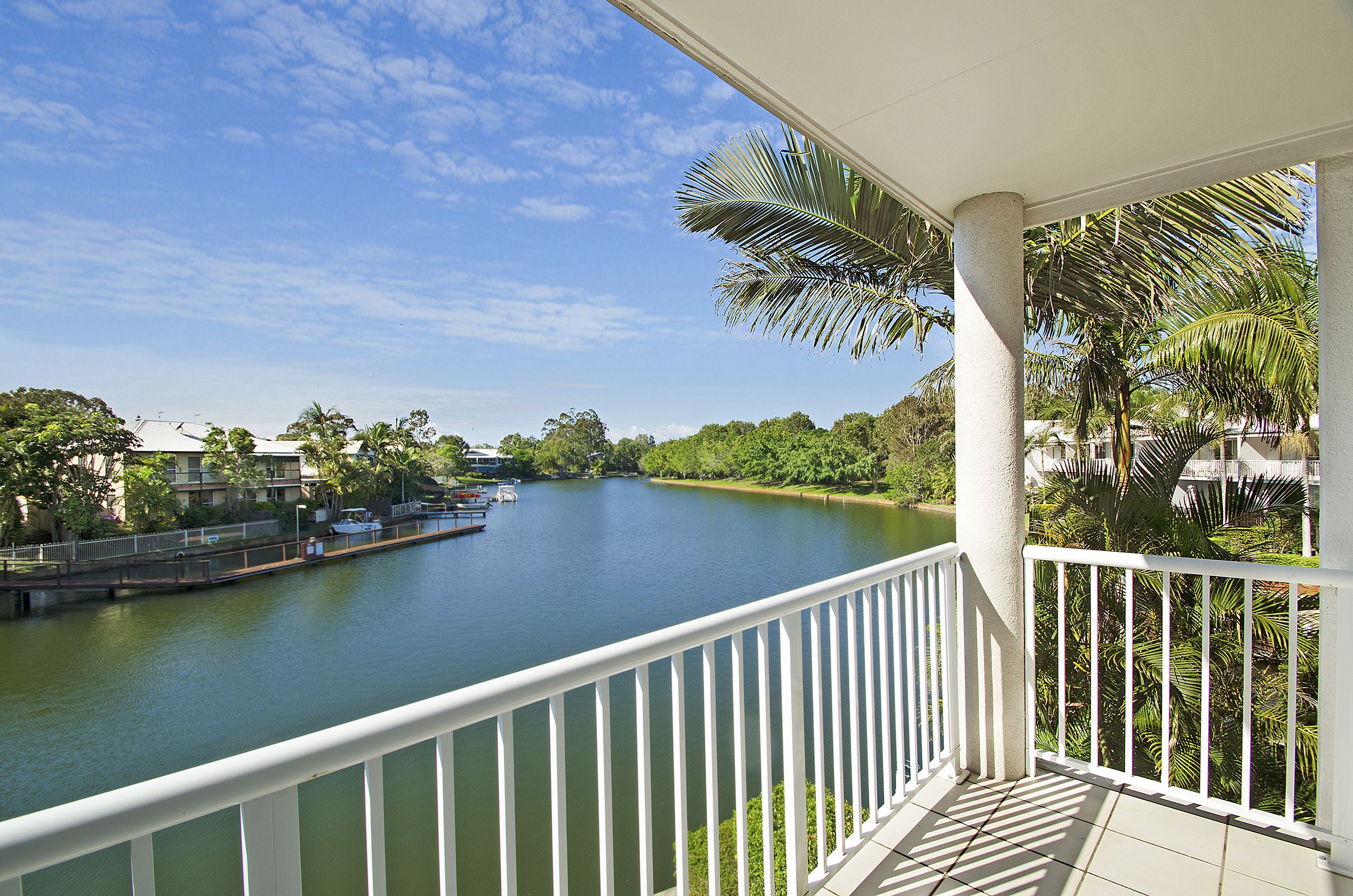 A balcony with a view of a calm river, surrounded by greenery and buildings.