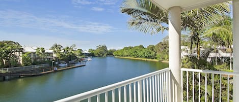 A balcony with a view of a calm river, surrounded by greenery and buildings.