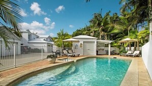 A swimming pool with lounge chairs and umbrellas, surrounded by palm trees and a white fence. - Portside Noosa Waters (Noosaville)