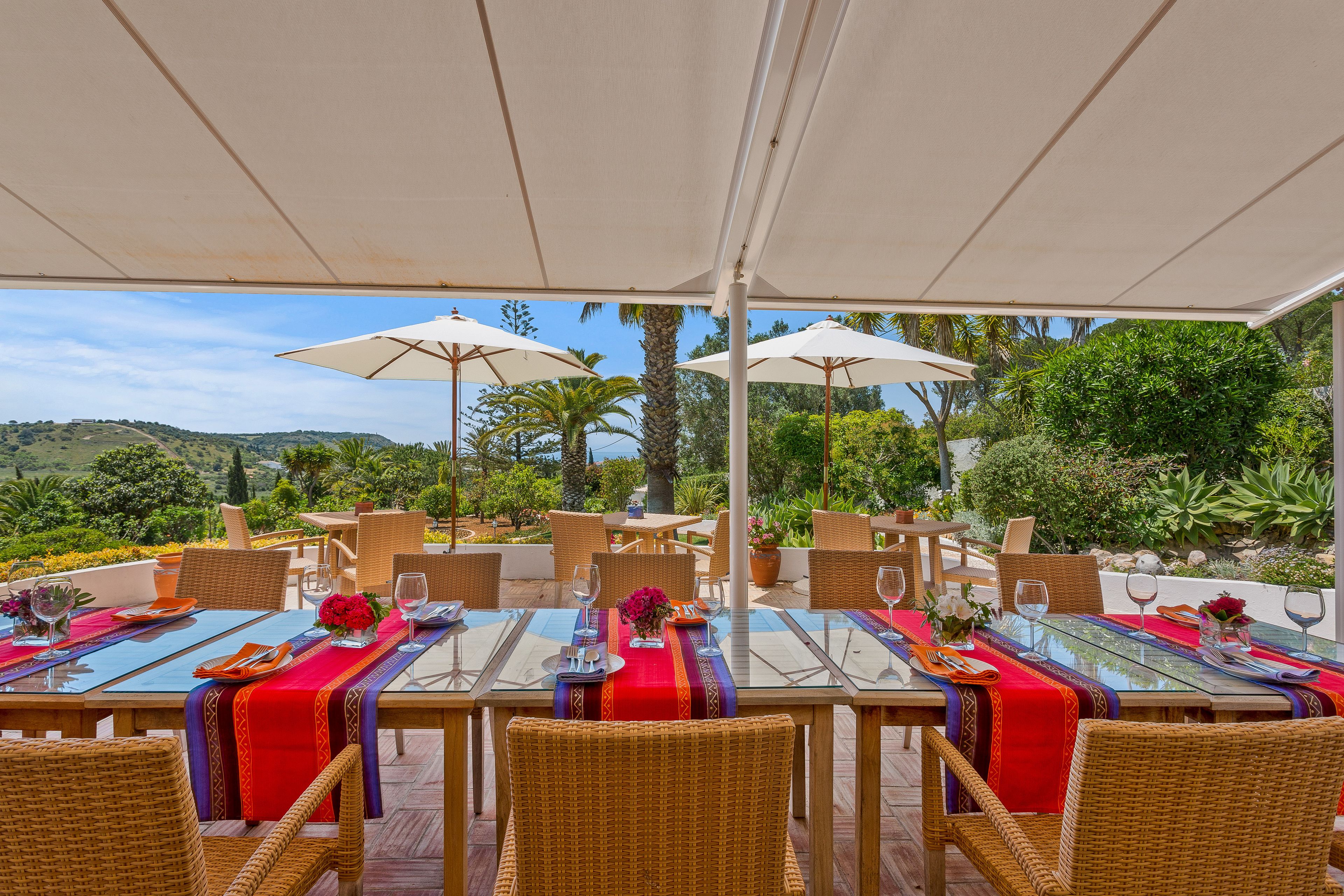 An outdoor dining area with tables and chairs, umbrellas, and a view of the landscape.