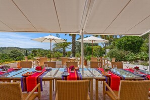 Un espace extérieur aménagé pour les repas, avec des tables, des chaises, des parasols et une vue sur le paysage.