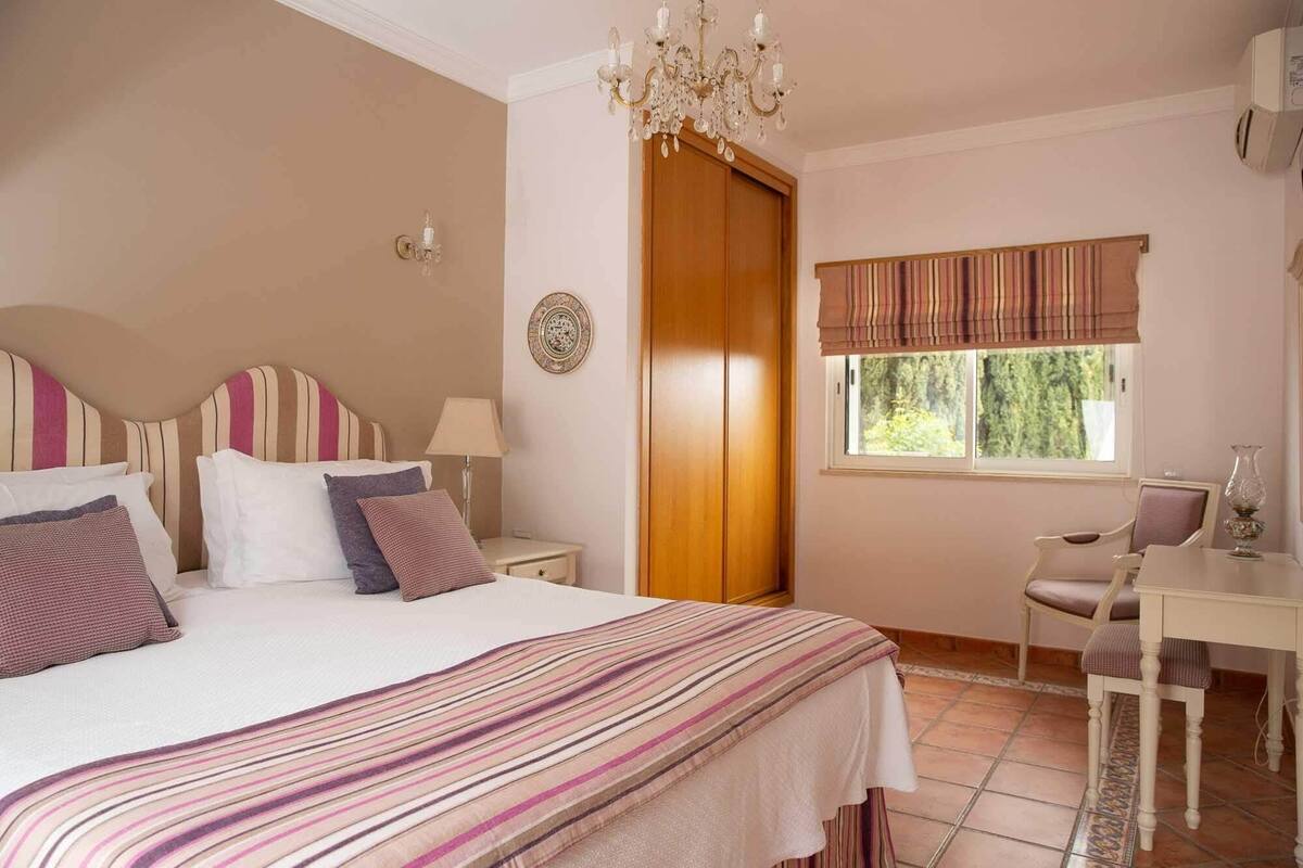 Un dormitorio con cama, mesita de noche, lámpara y ventana con cortinas.