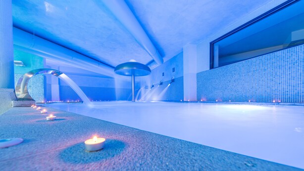 Un espacio interior moderno y amplio con iluminación azulada, una gran fuente de agua y una fila de velas en el suelo.