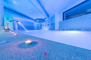 Un espacio interior moderno y amplio con iluminación azulada, una gran fuente de agua y una fila de velas en el suelo.