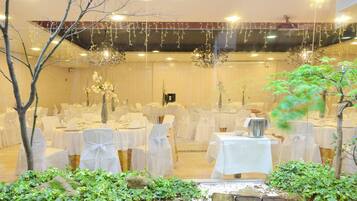 A banquet hall with tables set for a formal event, surrounded by greenery and decorative lighting.