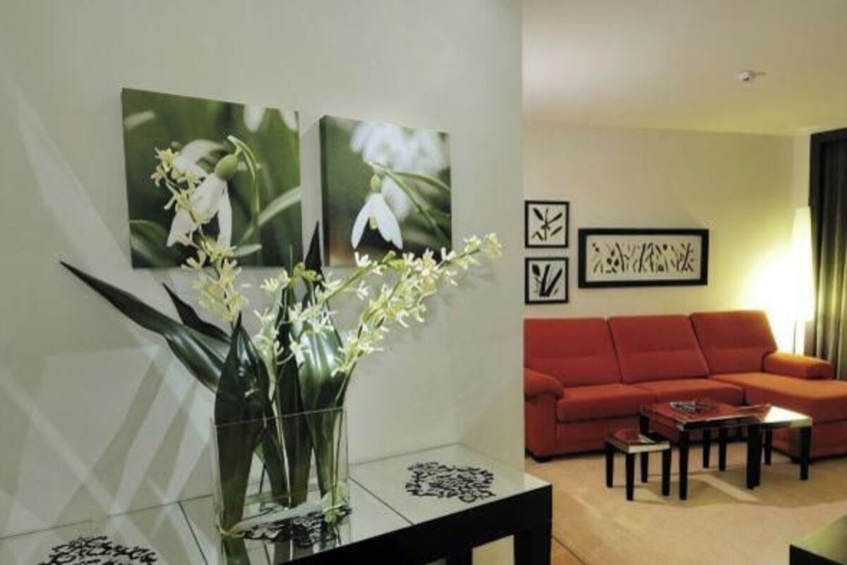A living room with a red sofa, a coffee table, and a vase with flowers. There are two framed pictures on the wall.