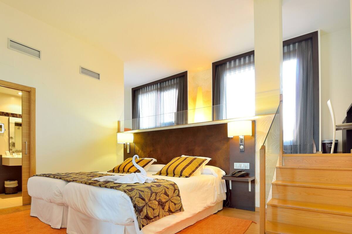 A hotel room with a bed, a nightstand, a lamp, a phone, and a staircase.