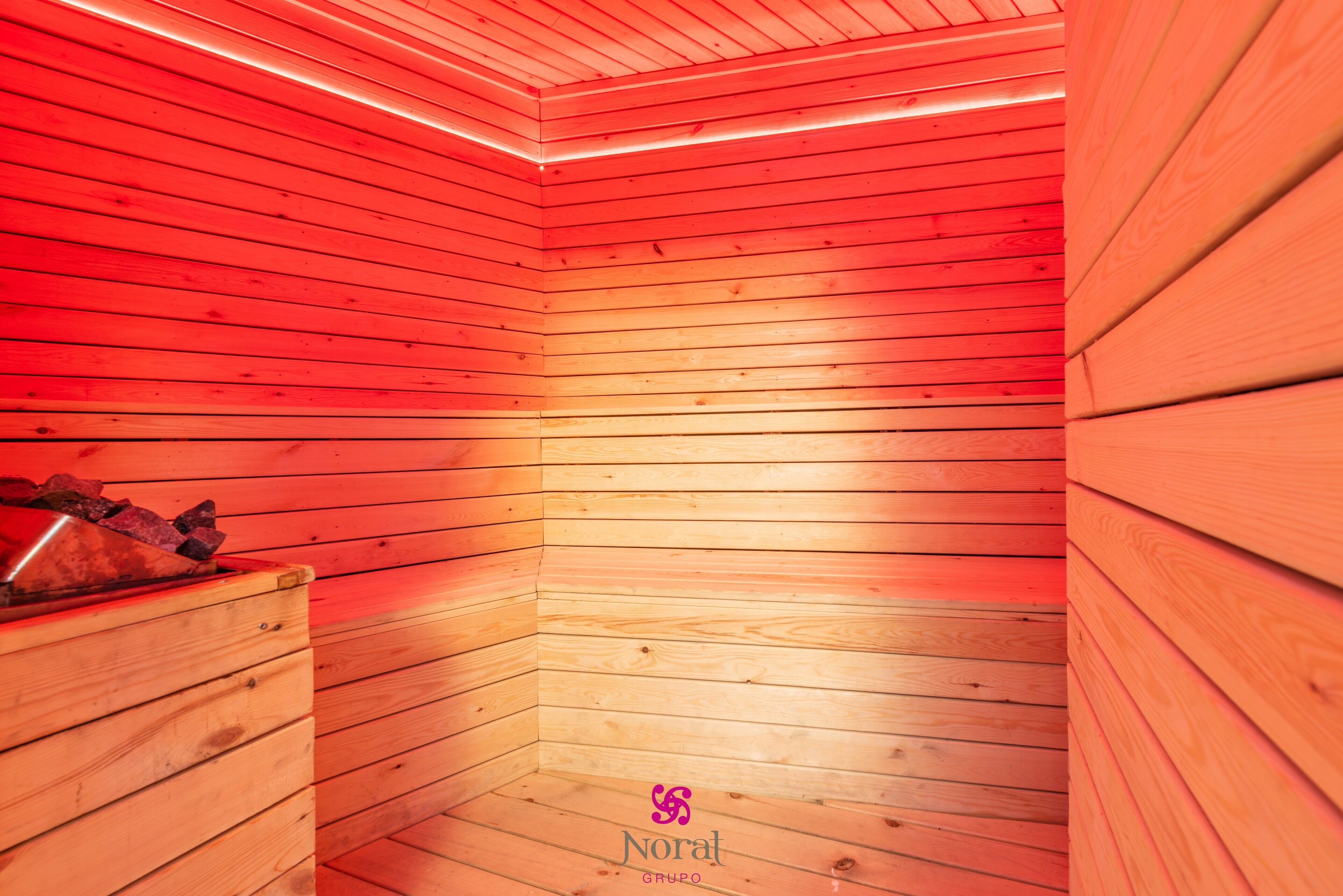 A sauna with wooden walls and a bench, featuring a logo at the bottom.