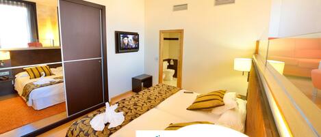 Habitación de hotel con cama, escritorio, silla, espejo y televisor.
