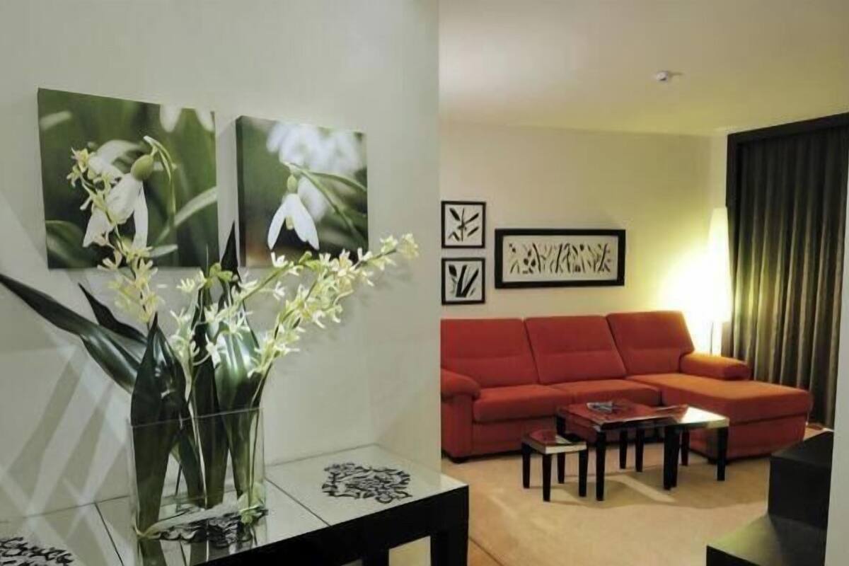 A living room with a red sofa, a coffee table, and a vase with flowers. There are two framed pictures on the wall.